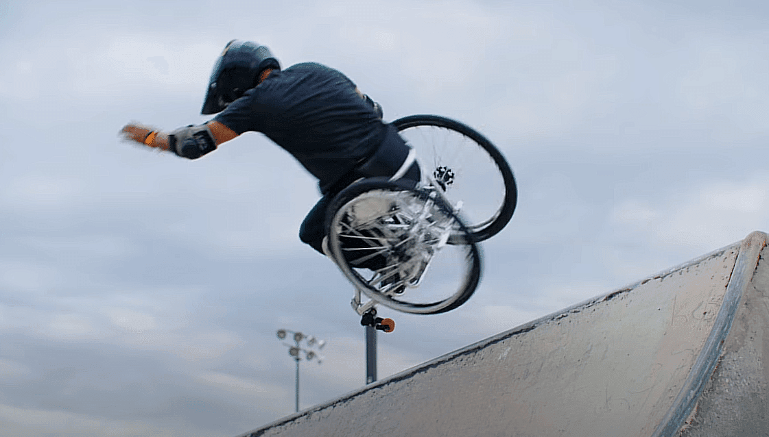 Un skateteur qui fait une figure de skateboard mais en fauteuil roulant